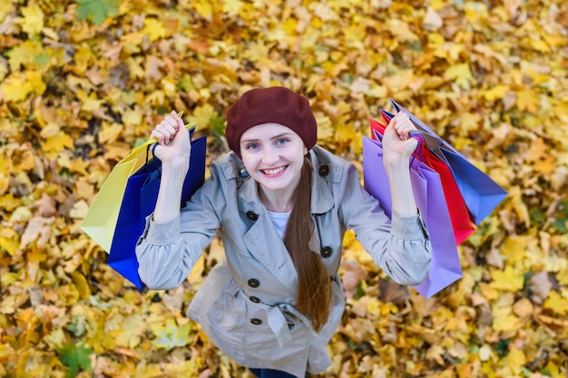 Felice bella giovane donna con borse della spesa su foglie autunnali sfondo concetto di consumatore vista dall'alto