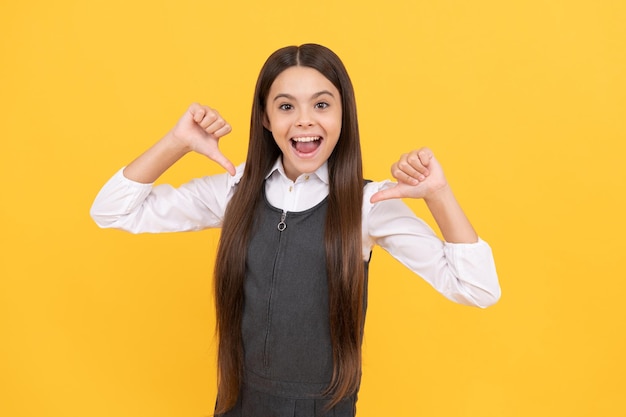 Happy primary school girl child smile pointing thumbs fingers yellow background education