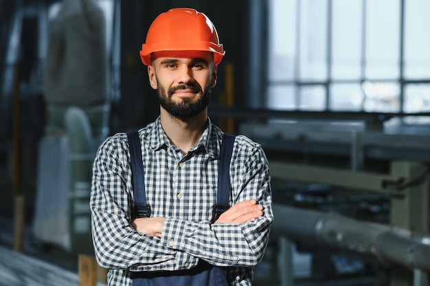 철강 공장에서 유니폼과 안전모를 착용하고 있는 행복한 전문 중공업 엔지니어 작업자 미소 짓는 산업 전문가가 금속 건설 제조에 서 있습니다