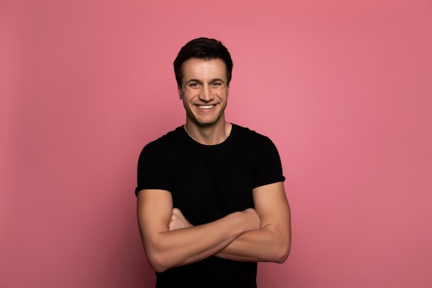 Happy and proud. handsome young man in a black t-shirt, who is standing with folded arms and smiling sincerely.