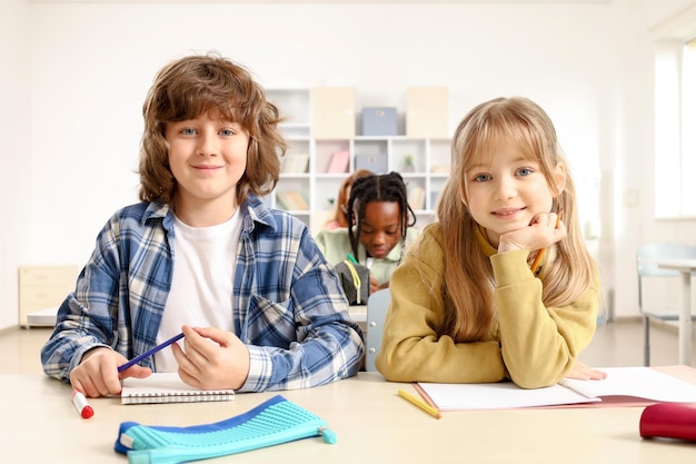 happy pupils sitting at desk in classroom while looking at camera education learning concept