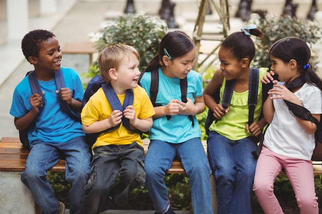 Happy pupils with schoolbags sitting on bench 