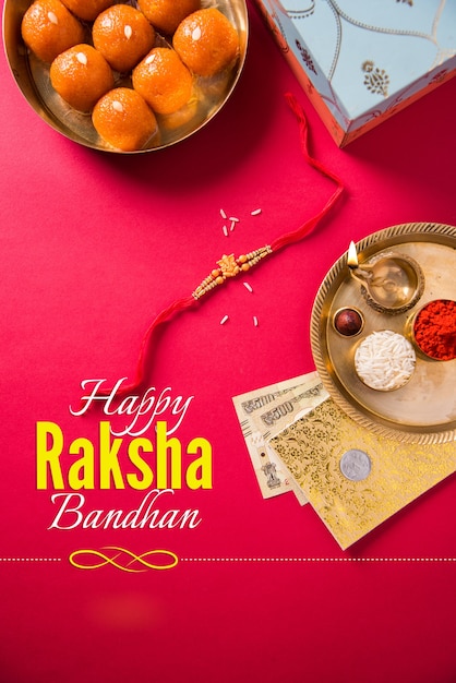 Фото happy raksha bandhan или rakhi greeting card с использованием дизайнерской нити, diya, pooja thali, подарочной коробки, индийских бумажных банкнот и сладостей и т. д. мрачное освещение, выборочный фокус