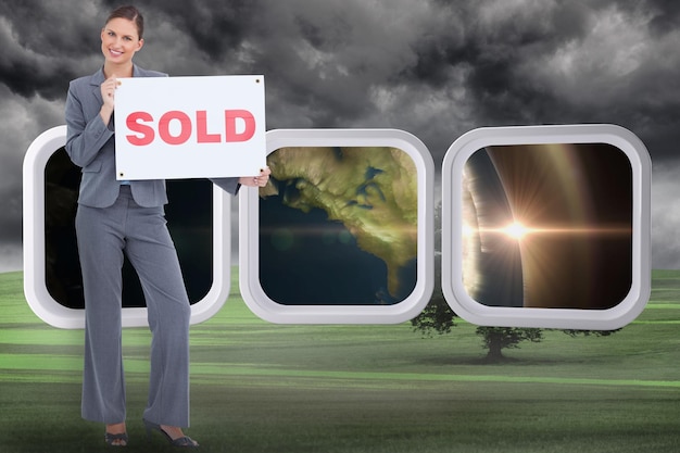 Happy real estate agent with sold sign against misty green\
landscape