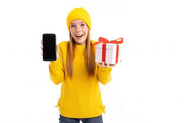 Happy red-haired girl with a phone and a gift in hands on a white 