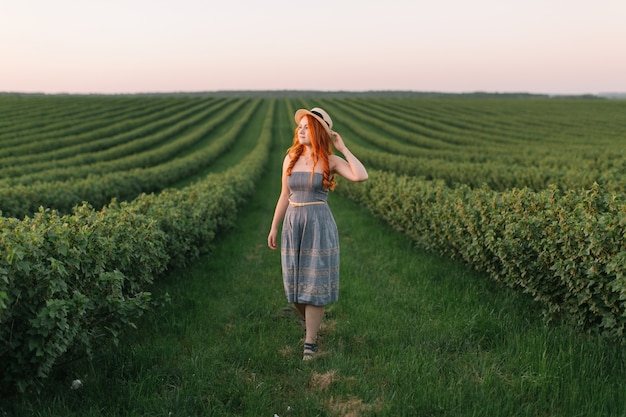 Happy red-haired woman in a hat on a green field