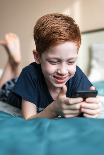 Happy redhaired child and digital technology the boy holds a phone in his hands writes messages