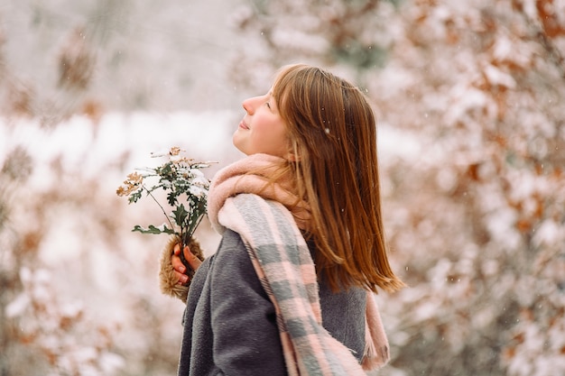 Фото Счастливая рыжеволосая девушка с зимним букетом в лесу. улыбается и смотрит в сторону. красота зимой