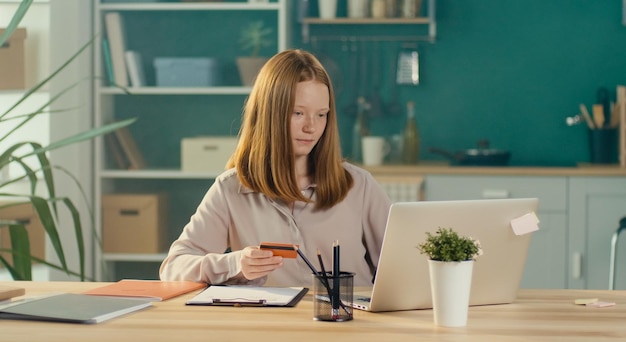 Фото Счастливая рыжеволосая девочка-подросток делает покупки в интернете с картой от домашнего потребителя