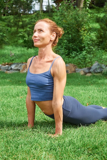 Happy redhaired woman in blue sportswear exercising outdoors in summer