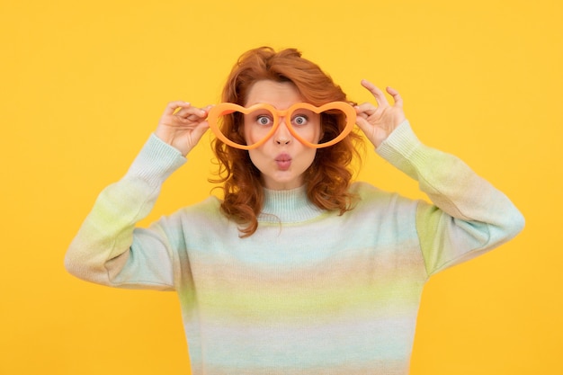 Happy redhead girl wear funny party glasses on yellow background, party.