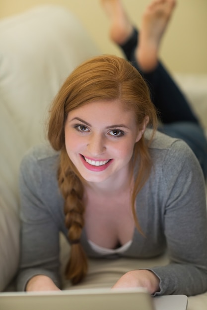 Photo happy redhead lying on the couch using her laptop at night