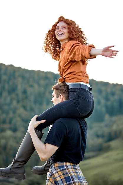 Happy redhead woman and guy trekking in mountains at summer. Positive couple hiking