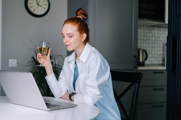 Happy redhead young woman having video call conversation using
laptop and drinking champagne. happy lady talking via webcam
gathering friends, boyfriend sending online congratulations.