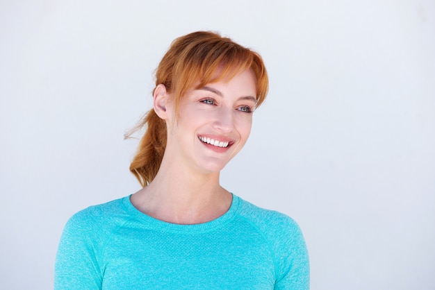 Happy redheaded woman smiling by white wall