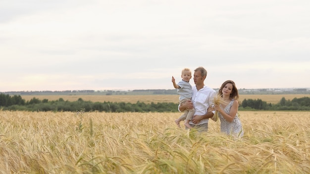 Happy relationship, young family walking together on a wheat field. Mother, father and little son leisures together outdoor. Parents and kid playing on summer meadow