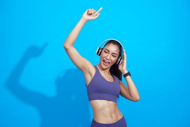 Happy relax asian woman using headphone listening music and dancing at fitness on blue background