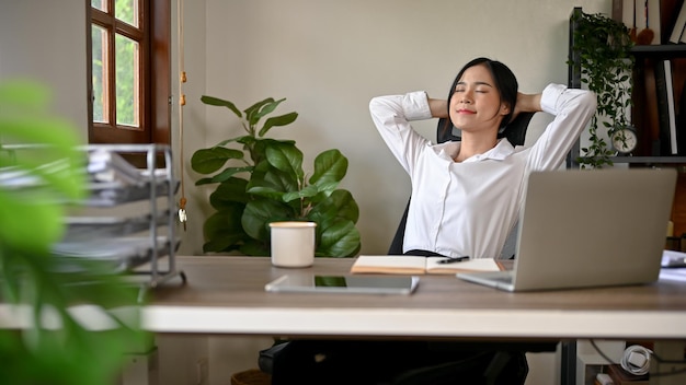 A happy and relaxed Asian businesswoman is leaning on her chair putting hands behind her head