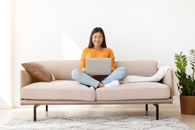 Happy relaxed chinese woman chilling at home using laptop