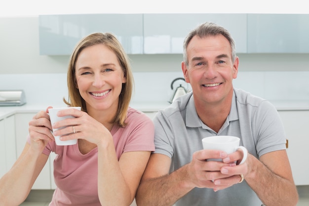 Happy relaxed couple with coffee cups in kitchen