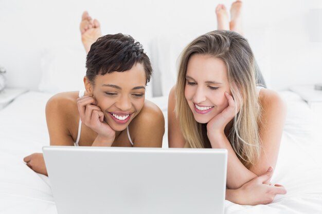 Happy relaxed friends using laptop in bed