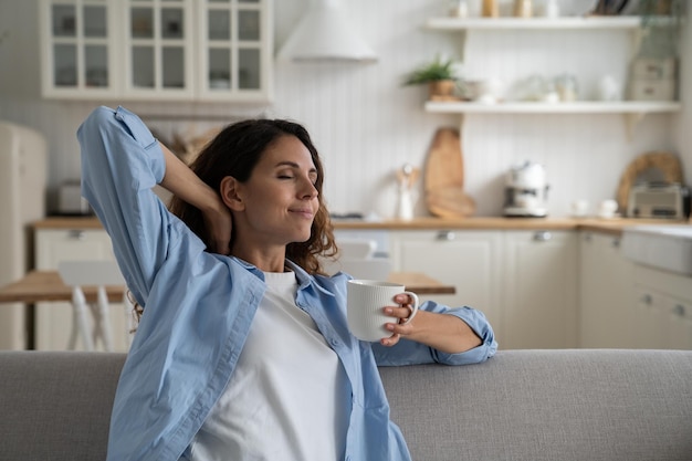 Happy relaxed woman holding cup of tea enjoying lazy day at home taking break from daily routine