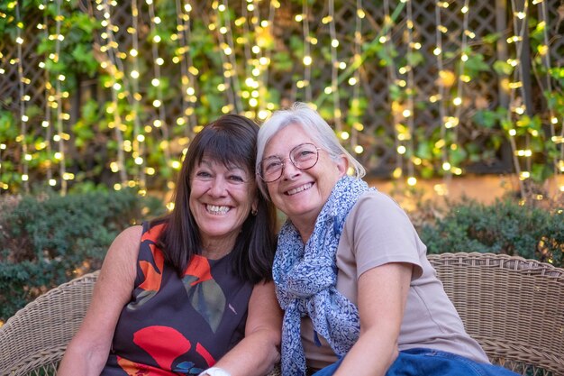 Photo happy relaxing moments for two aged mature senior women sitting outdoors embracing looking at camera