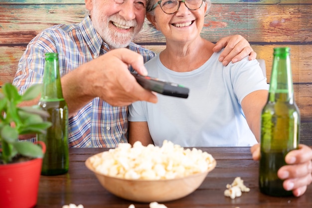 Felice coppia in pensione guardando la partita di calcio seduto al pub con due bottiglie di birra e un po' di popcorn. due anziani attraenti