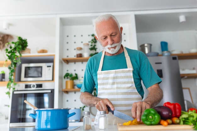 Happy retired senior man cooking in kitchen Retirement hobby people concept Portrait of smiling senior man cutting vegetables