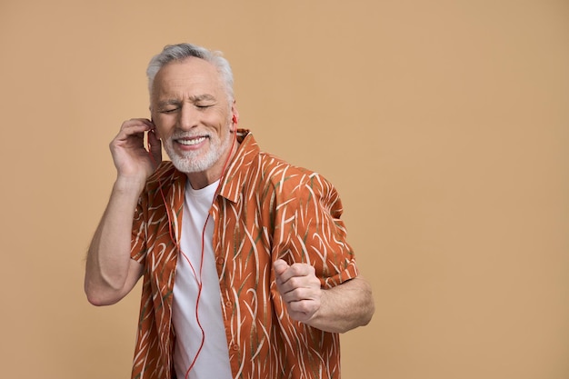 Happy retired senior man holiday maker enjoys summer vacation listens to music on beige background