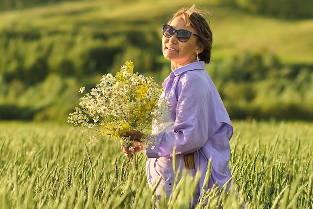 Happy retiree enjoying the day in a sunny park with wild flowers in her hands A symbol of active and joyful rest in nature in mature age