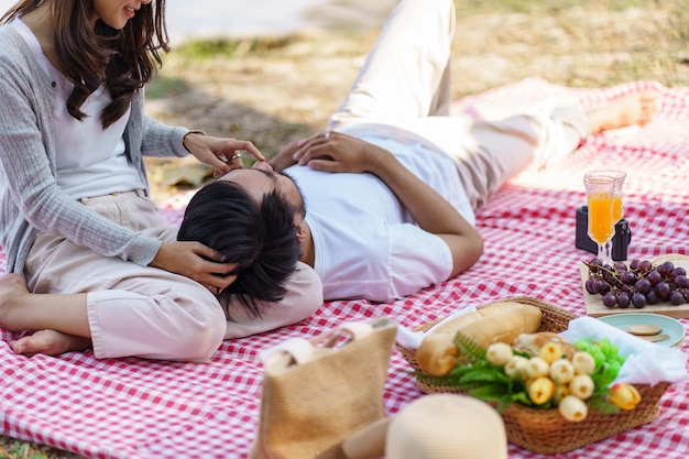 Happy romantic asian couple lying down at the park picnic time in summer holidays vacation