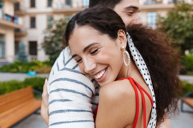 happy romantic couple in casual clothes laughing and hugging while walking on city street