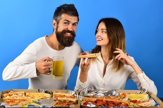 Happy romantic couple eating pizza drinks beer smiling family in kitchen tasting pizza food and