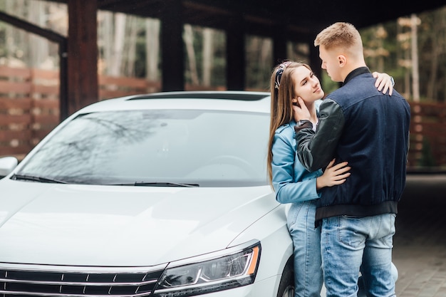 Happy romantic couple is standing near new car and house.