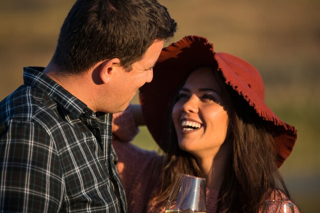 Happy romantic couple laughing and enjoying a glass of wine at sunset with lake behind them in the middle of a vineyard.