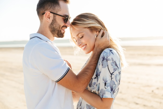 happy romantic couple man and woman smiling and hugging while walking on sunny beach