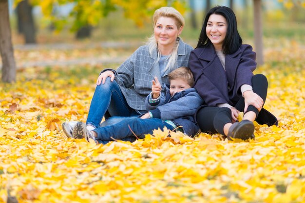 A happy same sex female couple and their son in a happy family theme with yellow fall leaves.