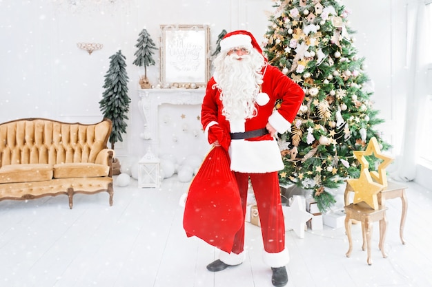 Happy Santa Claus binnenshuis in de buurt van de kerstboom met geschenken aan kinderen