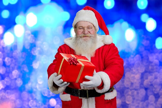 Happy Santa Claus holding red gift box.