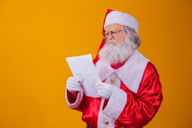 Happy Santa Claus holding vintage paper on yellow background. Merry Christmas and New Year's Eve concept. Copy space. Difficulty reading. Ugly handwriting.