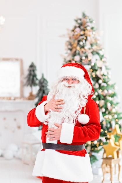 Happy Santa Claus indoors near christmas tree carrying gifts to children