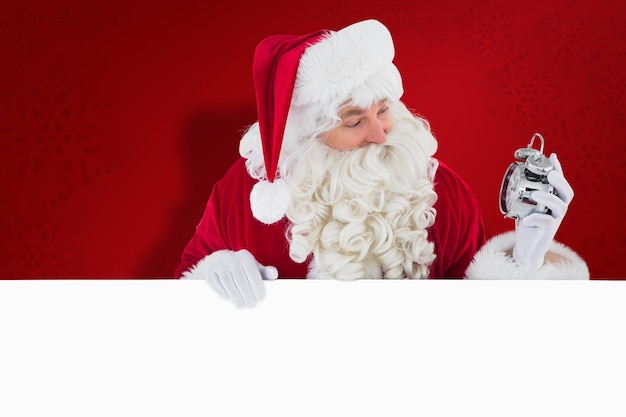 Happy santa holding alarm clock and sign against red snowflake background