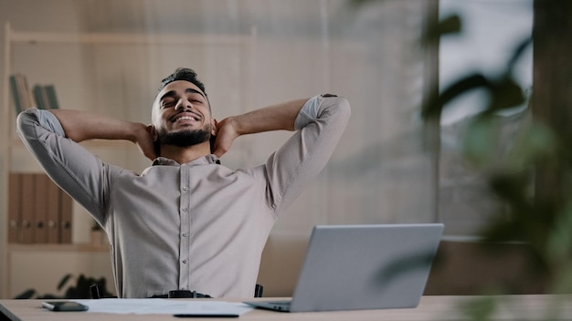 Happy satisfied arab man worker businessman hispanic guy finished work task on computer sit at home