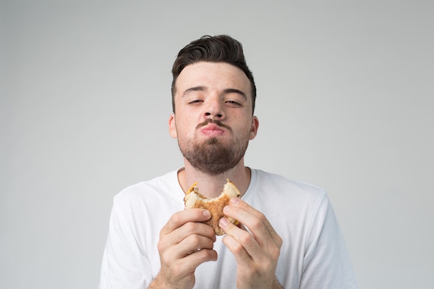 Happy satisfied guy look on camera and chewing burger. Eating bad fatning food with pleasure. Fastfood in hands.