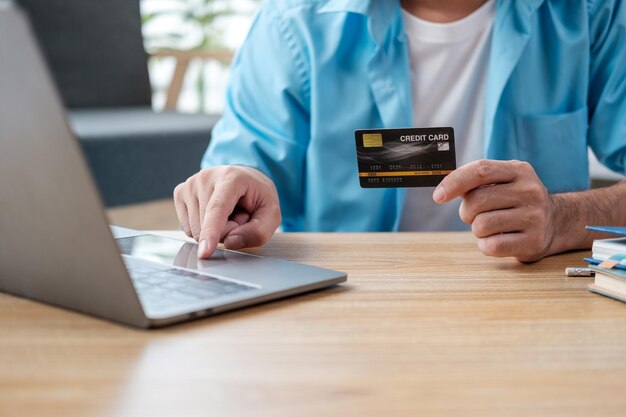 Photo happy and satisfied man shopping online sitting on sofa at home asian customer holding bank credit card and phone using online shopping app