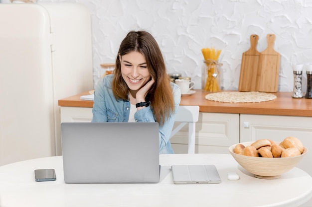 Happy satisfied woman working online using laptop in the kitchen in modern light apartment