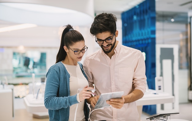 Happy satisfied young couple looking at new arrivals in tech store.