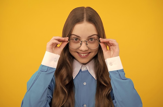 Happy school age girl child fix eyeglasses yellow background eyesight