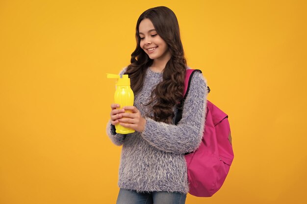 Счастливая школьница с книгами пьет бутылку воды в учебный день Вернуться к концепции школьного образа жизни Счастливый подросток позитивные и улыбающиеся эмоции школьницы-подростка